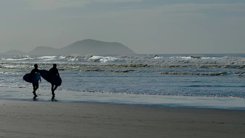 Dois surfistas em silhueta caminhando para o mar na Praia da Enseada em Bertioga